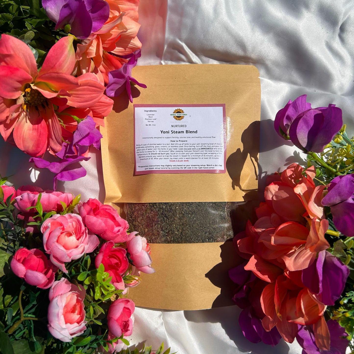 A kraft package of 'NURTURED' herbal yoni steam blend for uterine wellness surrounded by colorful flowers on a white surface
