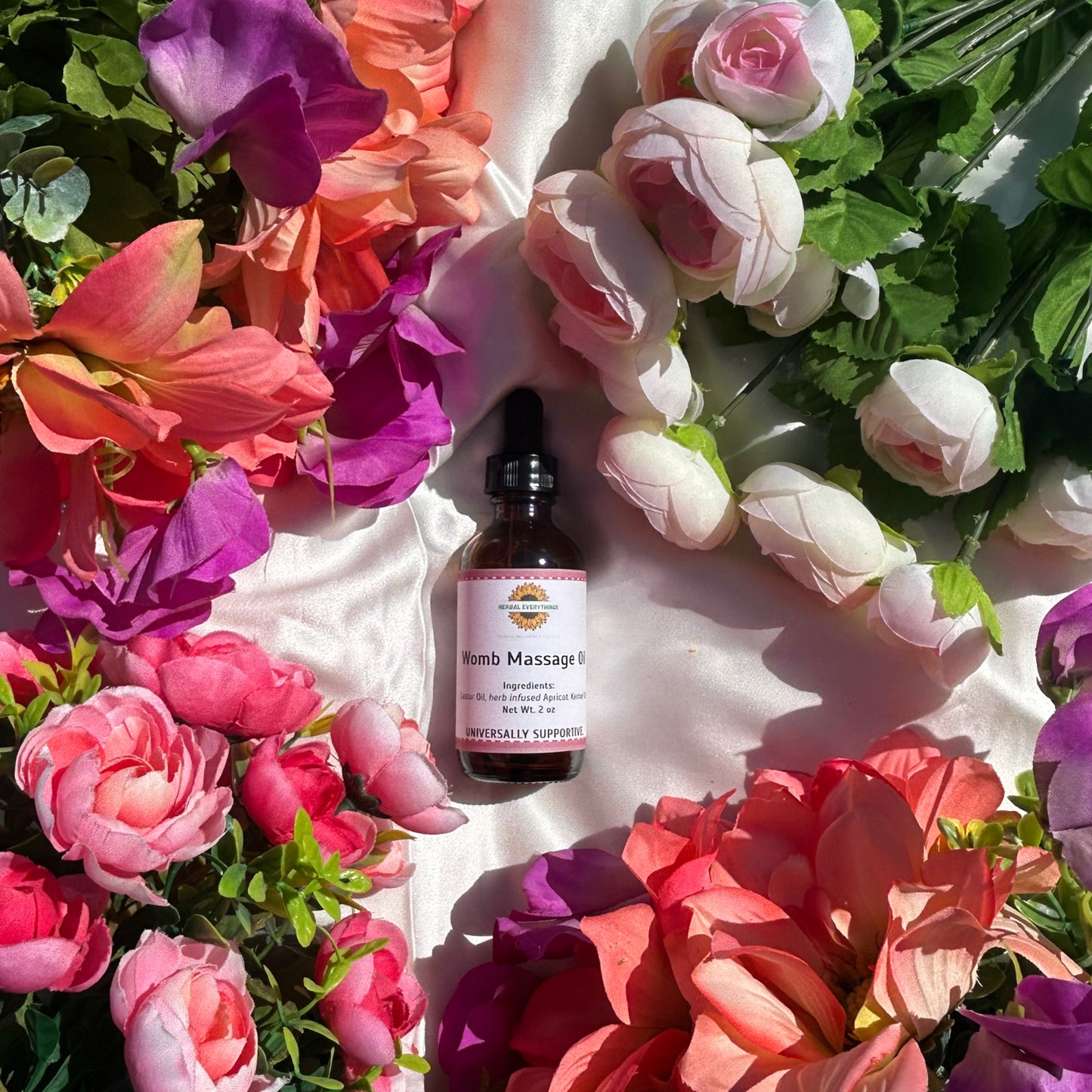 Bottle of Womb Massage Oil for pelvic circulation surrounded by colorful flowers on a white surface