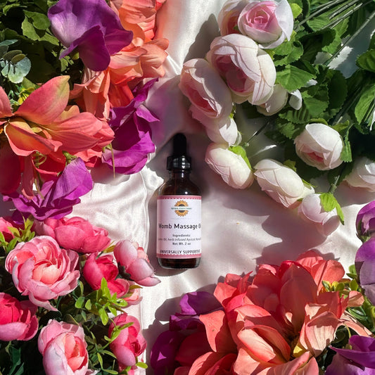 Bottle of Womb Massage Oil for pelvic circulation surrounded by colorful flowers on a white surface