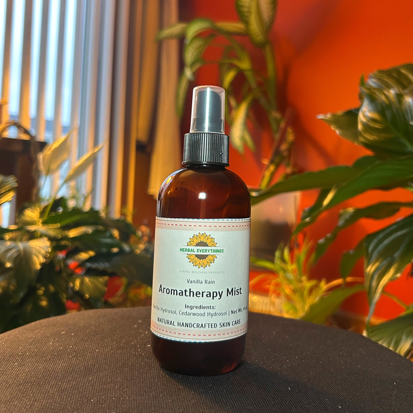 A spray bottle of vanilla aromatherapy mist for stress relief on a black surface with plants in the background